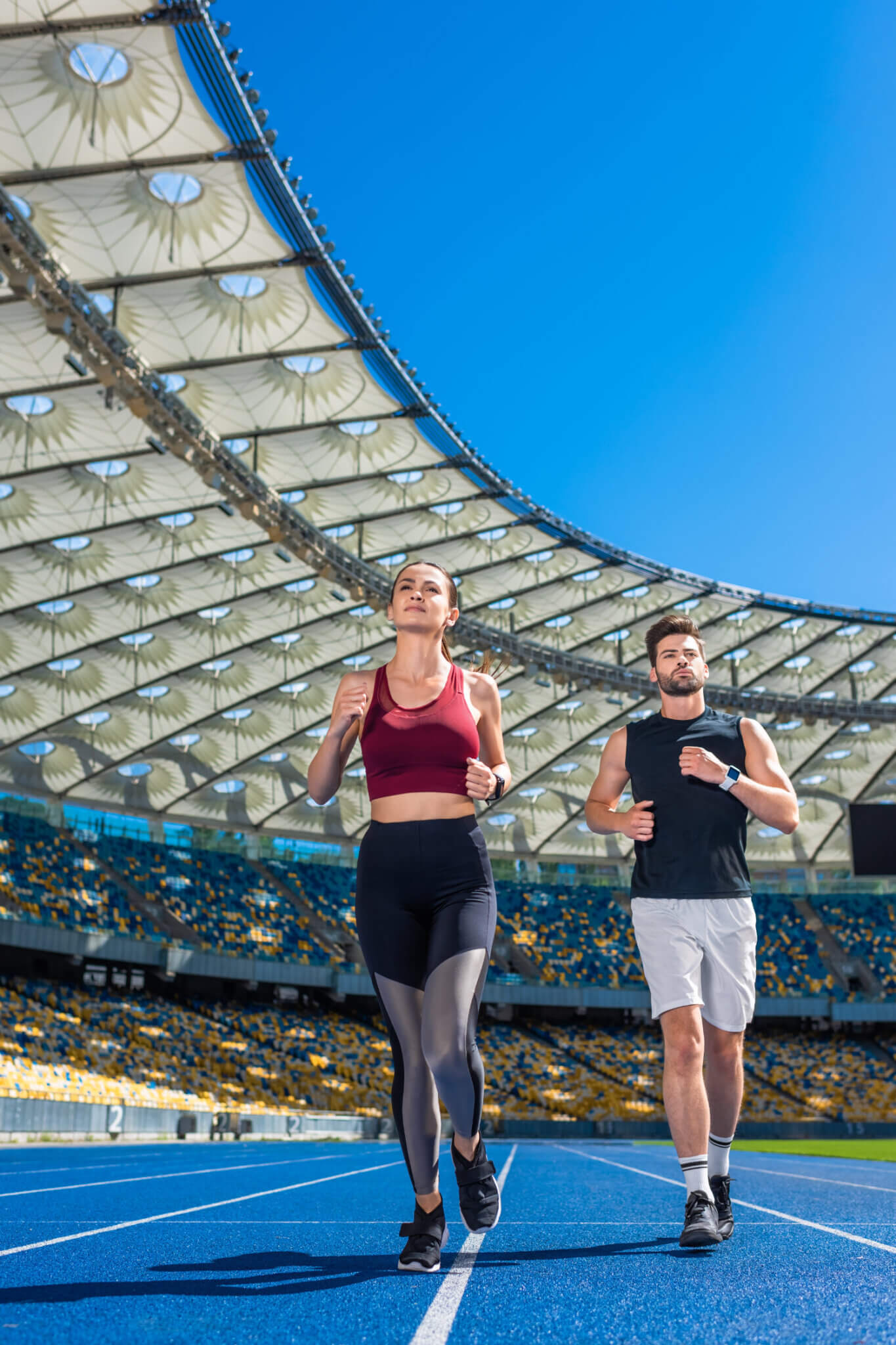 Fit Young Male And Female Joggers Running On Track At Sports Sta