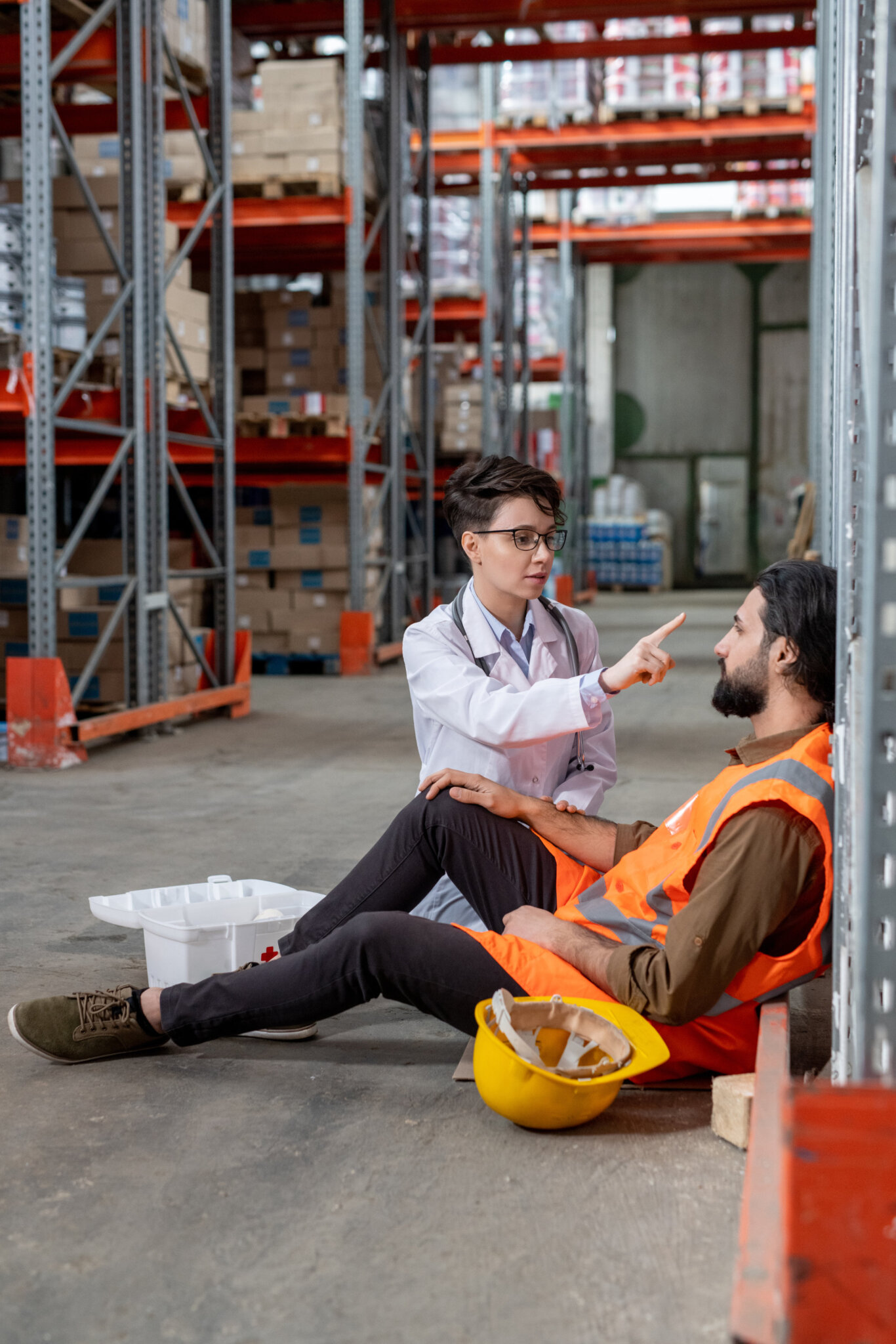 Young Doctor Sitting By Tired Or Sick Warehouse Worker